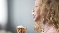 Happy blond girl eating creamy cupcake at birthday party, happy smiling child