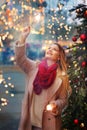 happy blond girl in winter coat and red scarf with sparklers portrait on decorated Christmas city background Royalty Free Stock Photo