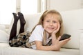 Happy blond little girl on home sofa using internet app on mobile phone Royalty Free Stock Photo