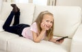 Happy blond little girl on home sofa using internet app on mobile phone Royalty Free Stock Photo