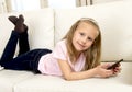 Happy blond little girl on home sofa using internet app on mobile phone Royalty Free Stock Photo