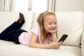 Happy blond little girl on home sofa using internet app on mobile phone Royalty Free Stock Photo