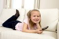 Happy blond little girl on home sofa using internet app on mobile phone Royalty Free Stock Photo