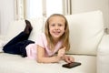 Happy blond little girl on home sofa using internet app on mobile phone Royalty Free Stock Photo