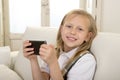 Happy blond little girl on home sofa using internet app on mobile phone Royalty Free Stock Photo