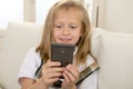 Happy blond little girl on home sofa using internet app on mobile phone Royalty Free Stock Photo