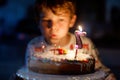 Happy blond little kid boy celebrating his birthday. Child blowing seven candles on homemade baked cake, indoor