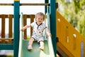 Happy blond little toddler girl having fun and sliding on outdoor playground. Positive funny baby child smiling. Royalty Free Stock Photo