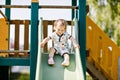 Happy blond little toddler girl having fun and sliding on outdoor playground. Positive funny baby child smiling. Summer Royalty Free Stock Photo