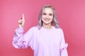 Happy blond model showing by finger up sstanding in the pink studio isolated.