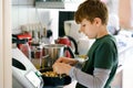 Happy blond school kid boy baking plum cake in domestic kitchen, indoors. Funny lovely healthy preteen child having fun