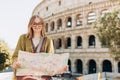 A happy blond woman tourist with paper map is standing near the Coliseum, old ruins at the center of Rome, Italy Royalty Free Stock Photo