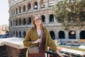 A happy blond woman tourist is standing near the Coliseum, old ruins at the center of Rome, Italy. Concept of traveling Royalty Free Stock Photo