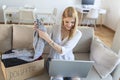 Happy blond young woman sit on couch stuck clothes in donation box at home, caring biracial female volunteer put apparel in carton Royalty Free Stock Photo