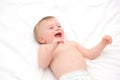 Happy blonde caucasian baby girl about 1 year old laughing lying on back on white bedlinen.Infant having fun before