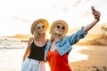 Happy blonde caucasian female friends having fun on vacation, taking selfie on the beach with a smart phone during beautiful Royalty Free Stock Photo