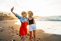 Happy blonde caucasian female friends having fun on vacation, taking selfie on the beach with a smart phone during beautiful Royalty Free Stock Photo