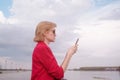 Happy blonde caucasian girl in sunglasses and a pink jacket on a background of river shore. Royalty Free Stock Photo