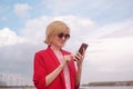 Happy blonde caucasian girl in sunglasses and a pink jacket on a background of river shore. Royalty Free Stock Photo