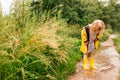 Happy blonde child girl in a yellow rubber boots and yellow raincoat staying in a puddle. Summer, childhood, holiday Royalty Free Stock Photo