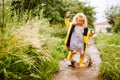 Happy blonde child girl in a yellow rubber boots and yellow raincoat jumping in a puddle. Summer, childhood, holiday