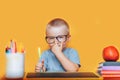 Happy blonde clever boy is sitting at a desk in glasses and smiling. Ready for school. Back to school. Apple, pens and books on Royalty Free Stock Photo