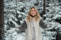 Happy blonde girl with blue eyes throws snow flakes from her hands. Beautiful portrait with bokeh in the winter forest.