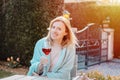 Happy blonde girl enjoying red wine outdoors. Smiling attractive joyful woman in light blue knitted plaid smiling and looking at g Royalty Free Stock Photo