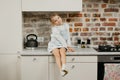 A happy blonde girl with pale skin is posing while sitting on the table in the kitchen