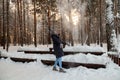 A happy blonde girl is standing in the winter forest on the background wooden bench in the snowdrifts playfully throws high to the Royalty Free Stock Photo