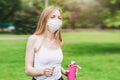 Happy blonde girl in a white medical mask smiles and runs through the park does fitness and physical activity quarantines in the