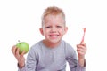 Happy blonde kid boy smiling with green apple and toothbrush on white background. Health care, dental hygiene, brushing