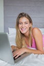 Happy blonde lying on her bed using her laptop Royalty Free Stock Photo