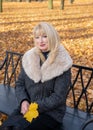 Happy blonde mature woman is sitting on bench in autumn park and thinking. Beautiful woman is relaxing in nature on sunny day. Royalty Free Stock Photo