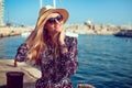 Happy blonde mediterranean woman in hat posing at sea in city