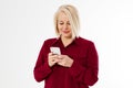 Happy blonde middle aged woman in red suit isolated on white background holding phone