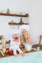 Caucasian blonde mother and little daughter in white cap eat apple in kitchen.