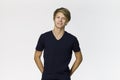 Happy blonde teenager posing in blue t-shirt with hands in his pockets against white wall Royalty Free Stock Photo