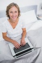 Happy blonde woman in bed using her laptop Royalty Free Stock Photo