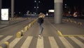 Happy blonde woman having fun outdoors at the nighttime. Running, immitating plane. Wearing jeans and black jacket. Rare