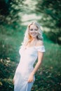 Happy blonde woman in white summer dress walks in park. Fashion