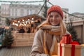 Happy blonde woman in winter coat holding a gift box at Christmas market. Attractive happy girl shopper hold gift boxes Royalty Free Stock Photo