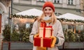 Happy blonde woman in winter coat holding a gift box at Christmas market. Attractive happy girl shopper hold gift boxes Royalty Free Stock Photo