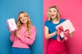 Blonde women holding gift boxes with bows on blue and pink background Royalty Free Stock Photo