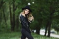 Happy blonde young woman with trendy makeup, in a black leather jacket and black hat, over a green background with bokeh Royalty Free Stock Photo