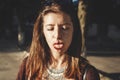 Happy boho carefree girl showing tongue and smiling in sunny street. Stylish bohemian girl with fashionable look having fun in