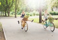 Happy boho chic girls ride together on bicycles in park