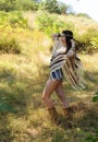 Happy boho style woman dressed in knitted poncho, jeans shorts and headband Royalty Free Stock Photo
