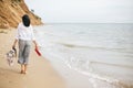 Happy boho woman relaxing at sea, enjoying walk on tropical island. Stylish hipster girl walking barefoot on beach, holding bag Royalty Free Stock Photo