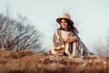 Happy boho woman sitting at sunset in mountains, wearing hat and